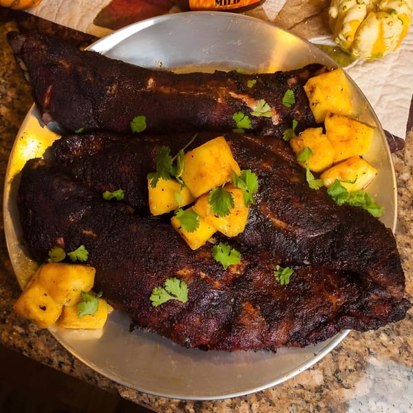 Two racks of Bill's Grill Smokehouse ribs, garnished with pineapple chunks and cilantro, on a metal tray.