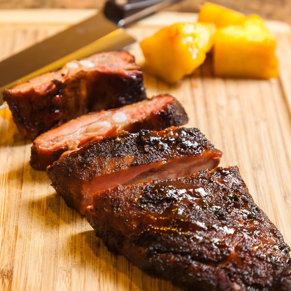 Close-up of Bill's Grill Smokehouse BBQ ribs, sliced on a wooden cutting board with pineapple.