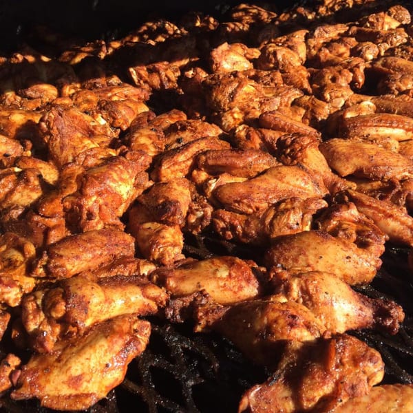 Close-up of numerous seasoned chicken wings and drumsticks cooking on a grill at Bill's Grill Smokehouse.