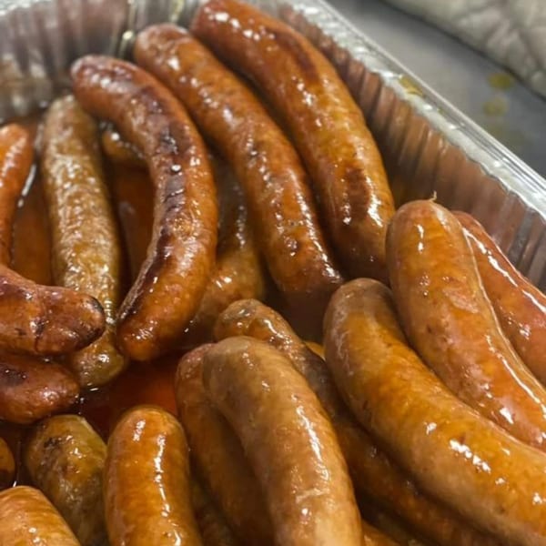Close-up of glistening, brown sausages in a metal tray, likely from Bill's Grill Smokehouse.