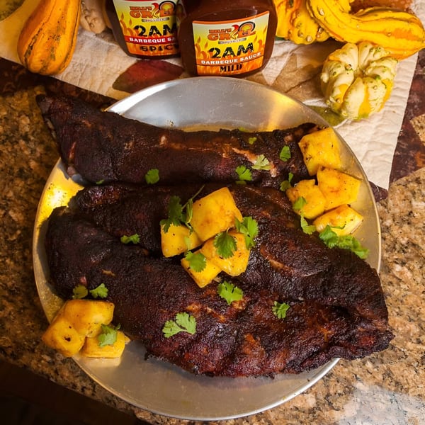 Bill's Grill Smokehouse ribs with pineapple and cilantro, with two bottles of BBQ sauce in the background.